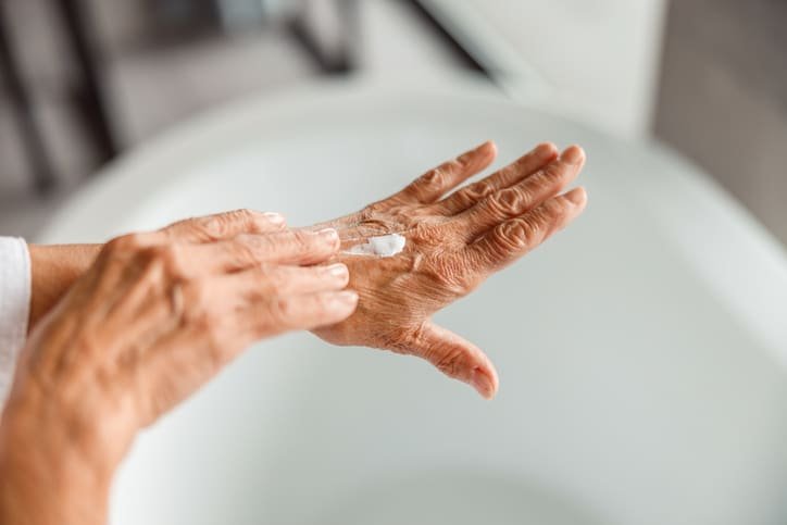 An older person applying moisturising cream to the back of one hand, illustrating gentle daily skin care for ageing skin.